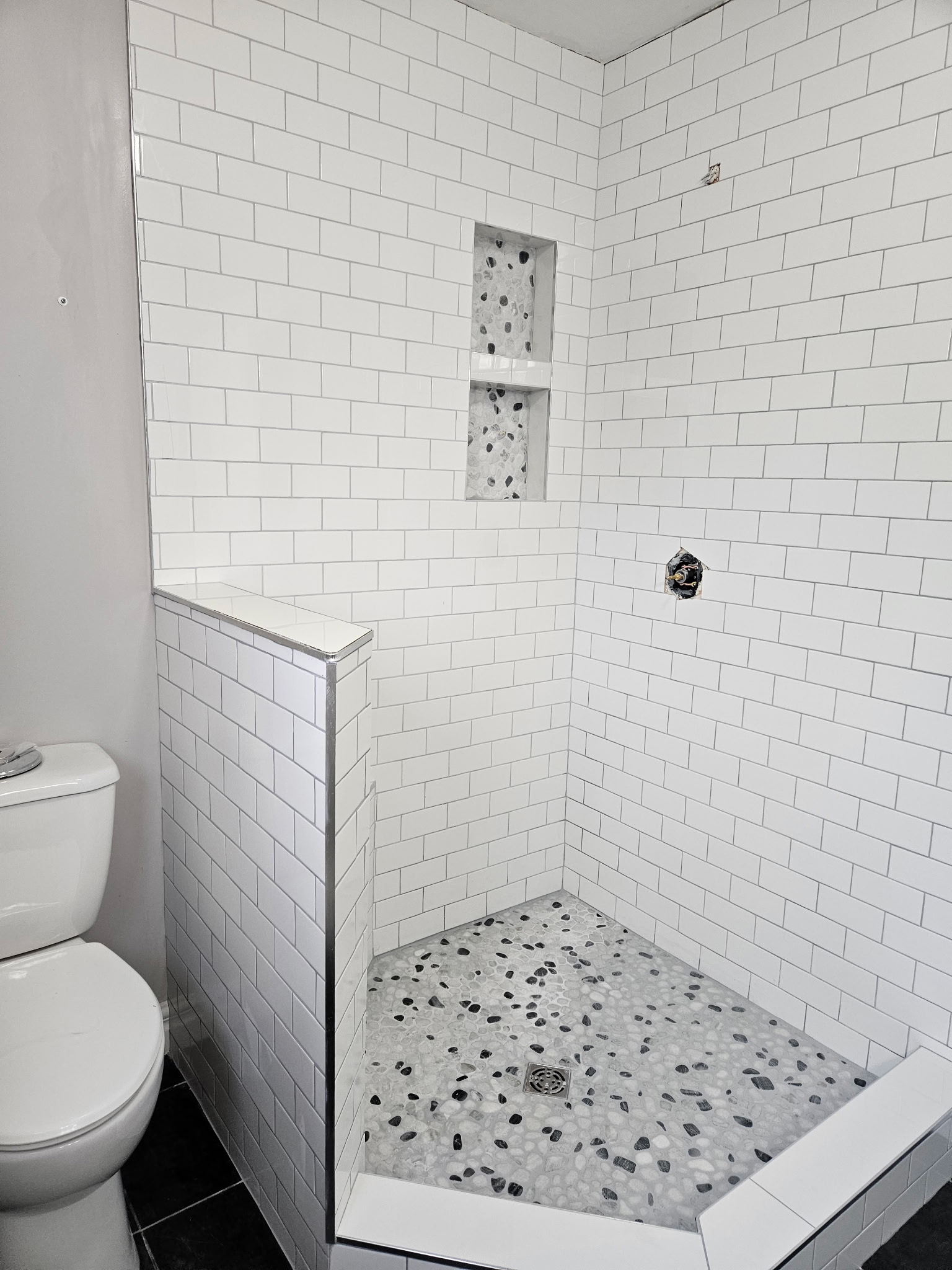 Custom tiled walk-in shower with pebble floor and recessed shelves